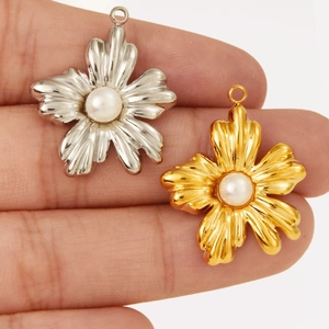 Close-up of small flower pendants in gold and silver with white pearls held by fingers