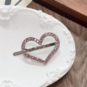 Detail of a silver heart hair clip with pink rhinestones on a vintage relief plate