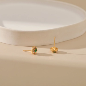 Close-up of gold halo stud earrings with green gemstones and sparkling zircon details