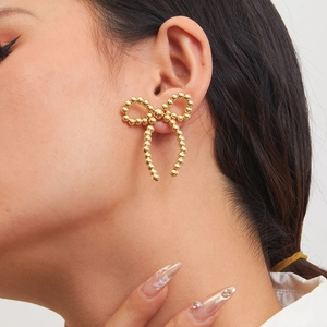 Close-up of elegant gold bow earrings with beaded texture worn on a model's ear