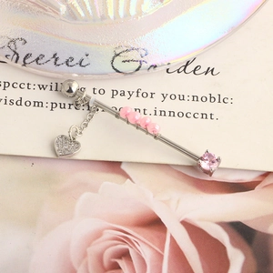 Macro detail of industrial barbell earring with pink beads and a heart-shaped diamond charm