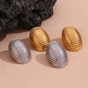 Detail of gold and silver oval ribbed stud earrings on a textured stone surface
