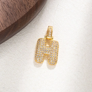 Macro detail of gold letter H pendant with micro-pave cubic zirconia on textured wood