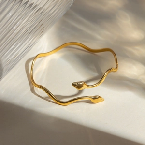 Detail of 18k gold plated stainless steel double snake head open bangle with elegant shadows