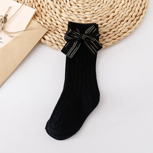 Detail of black knit baby socks with gold-striped bow on minimalist white background