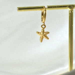 Detail of 14K gold plated starfish earrings with a textured pendant on white fabric