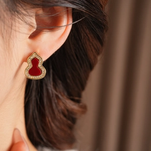 Detailaufnahme eines goldenen Calabash-Ohrrings mit rotem Inlay und klaren Kristallen