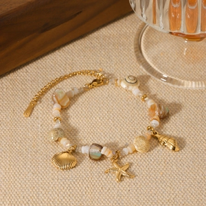 Gold ocean themed charm bracelet with seashells and starfish charms on a beige fabric backdrop