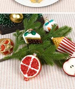 Close-up of assorted glass Christmas ornaments including pomegranate and cake on pine branches