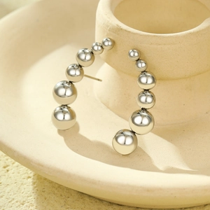Silver bead hoop earrings with gradient metal spheres on a ceramic display