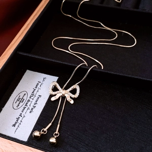 Macro shot of zircon bow pendant with long gold tassel balls on elegant snake chain