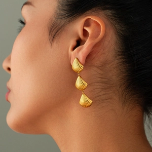 Close-up of a model wearing gold shell-shaped earrings with a triple-layered metal design