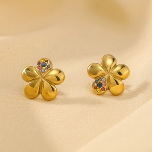 Macro detail of gold flower earrings with colorful gemstones on a beige fabric background