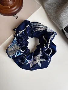 Macro detail of navy blue satin scrunchie featuring intricate starfish embroidery
