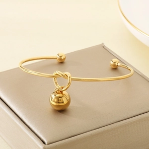 Detailed view of gold knot bangle with a smooth spherical pendant on a display