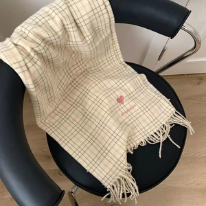 Close-up of beige plaid scarf with pink heart embroidery and tassels on a leather chair