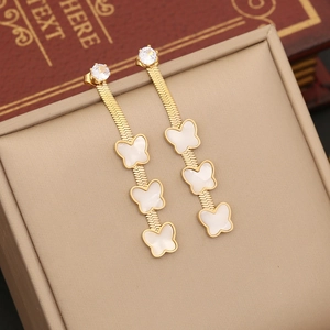 Detail of gold butterfly drop earrings with white charms on a vintage book background