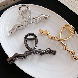 Three wavy metal hair claw clips in gold silver and black on a white ceramic tray