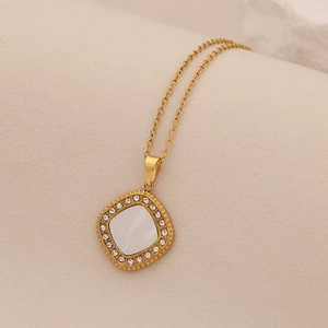 Gold pendant necklace with square white shell inlay and sparkling crystals on soft fabric