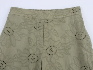 Close-up of olive green pants featuring intricate floral hollow embroidery and cotton texture