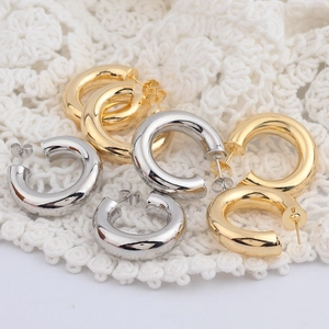 Détail macro de boucles d'oreilles créoles C dorées et argentées sur dentelle blanche