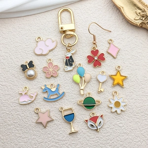 Mix of colorful enamel charms and golden earring hooks on beige textured fabric