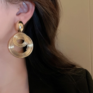 Close-up of a model wearing layered gold concentric circle geometric drop earrings