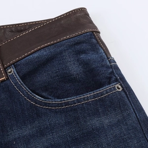 Détail du jean denim bleu foncé montrant le patch de taille en cuir marron et coutures