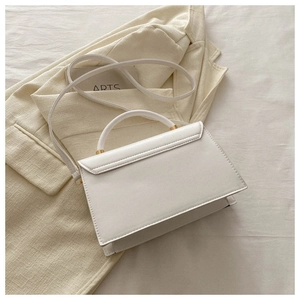 Détail d'un sac trapèze en cuir PU blanc avec finitions dorées sur un fond de ton beige