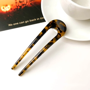 Detailed view of U-shaped tortoiseshell hair pin with polished acetate finish on white surface
