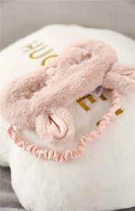 Detail of pink plush bunny sleep mask with soft fur texture on white pillow