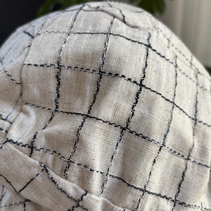 Close-up of a linen plaid beret hat with black checkered stitching on beige fabric