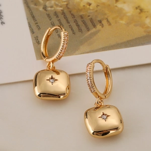 Créoles dorées avec pendentif carré et zircon en étoile sur une surface beige