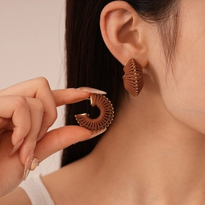Macro detail of brown leather twisted C-shape earrings with gold metallic thread accents