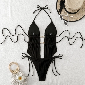 Detailed flat lay of black cutout bikini with seashell beads on a beach holiday background