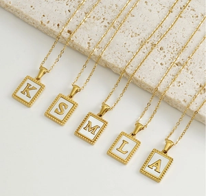 Detail of 18K gold stainless steel necklaces with white shell alphabet pendants on stone