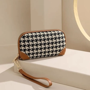 Detailed shot of houndstooth clutch bag with brown leather trim and golden zipper