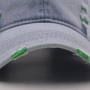 Detail of distressed denim baseball cap showing torn brim and green contrast lining
