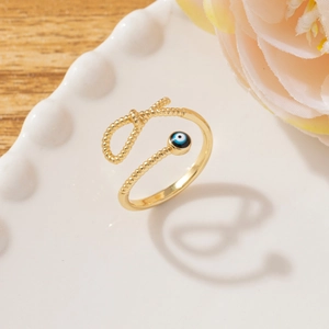 Detail of gold evil eye ring with twisted band on decorative plate and floral background