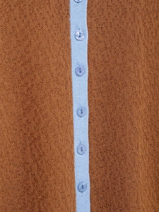 Detail aus ockerfarbenem Grobstrick mit hellblauer Knopfleiste und fünf Knöpfen