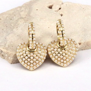 Macro shot of heart-shaped earrings with full micro pearl inlay on gold base