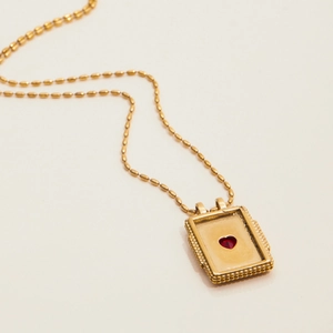 Detail of gold heart pendant with red stone and beaded edge on a dainty ball chain