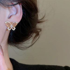 Close-up of elegant gold butterfly stud earring with sparkling zircons on a model's ear