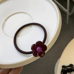 Détail d'un élastique à cheveux fleur marron café avec perle violette sur plateau blanc