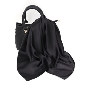 Elegant black silk satin square scarf draped on a leather handbag with smooth texture