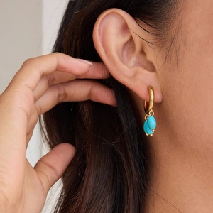 Detailed view of model wearing gold hoop earrings with turquoise bead dangles