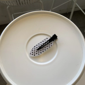 Detail shot of a black and white polka dot duckbill hair clip on a white plate