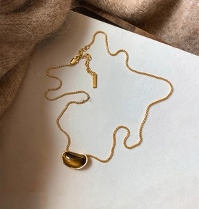 Detail of 18k gold plated tiger eye pea pendant on fine chain over knit sweater