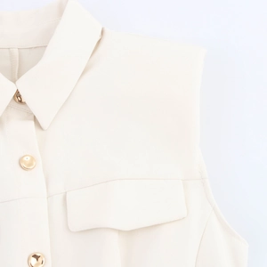 Detail of cream sleeveless dress featuring golden buttons and elegant lapel collar