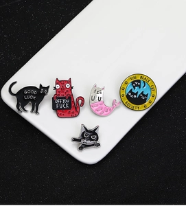 Macro shot of five creative cat enamel pins in colorful zinc alloy on a white ceramic tray